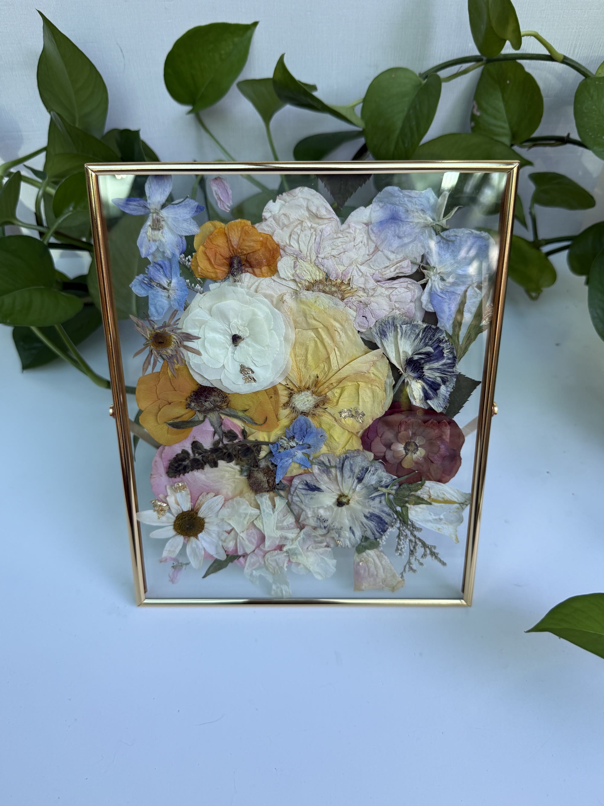 Colorful pressed wedding flowers in a gold frame